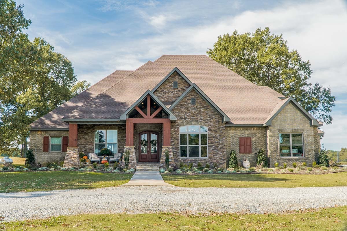 House plan exterior of a one-story home with stone and brick facade, covered front porch with timber supports, and multiple gables.