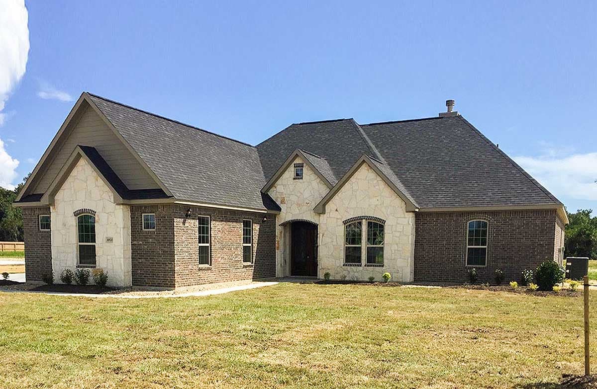 House plan exterior: One-story home with brick and stone facade, arched entry, gables, and dark pitched roof.