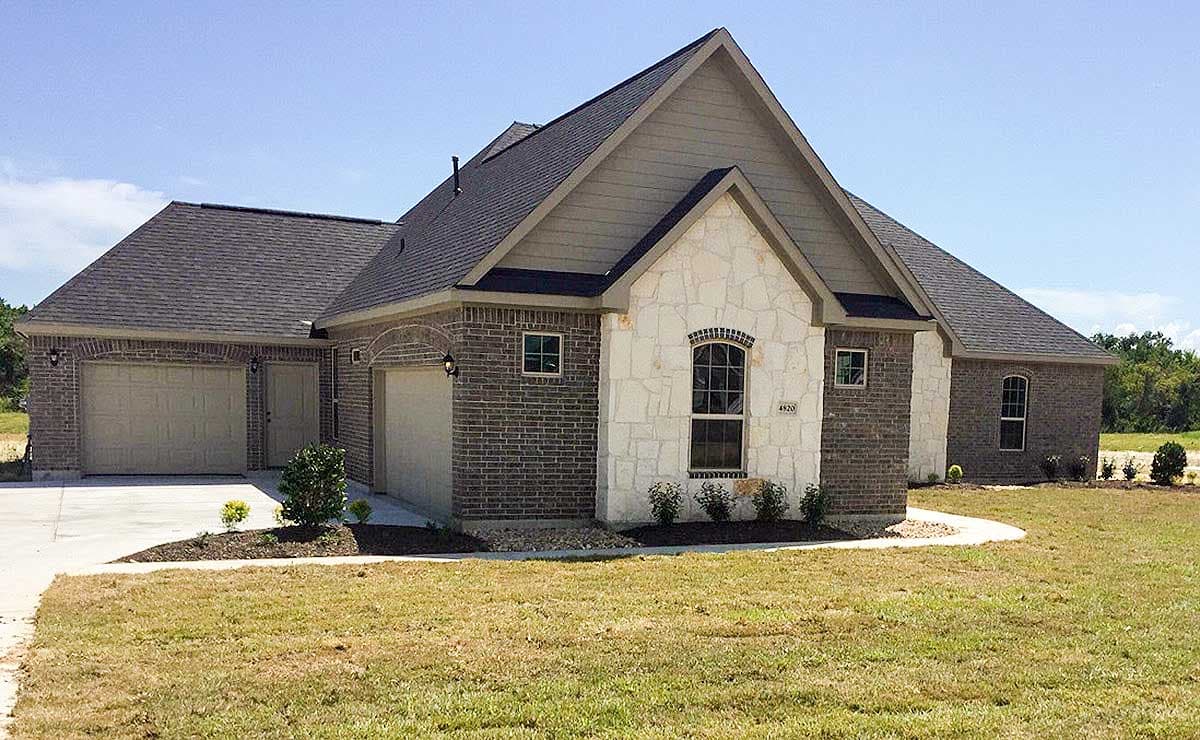 House plan exterior with a brick facade, white stone accents, gabled rooflines, and a three-car garage.