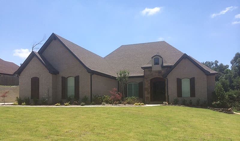 One-story house plan exterior with brick facade, gabled rooflines, arched windows, stone accents, and a covered entry.