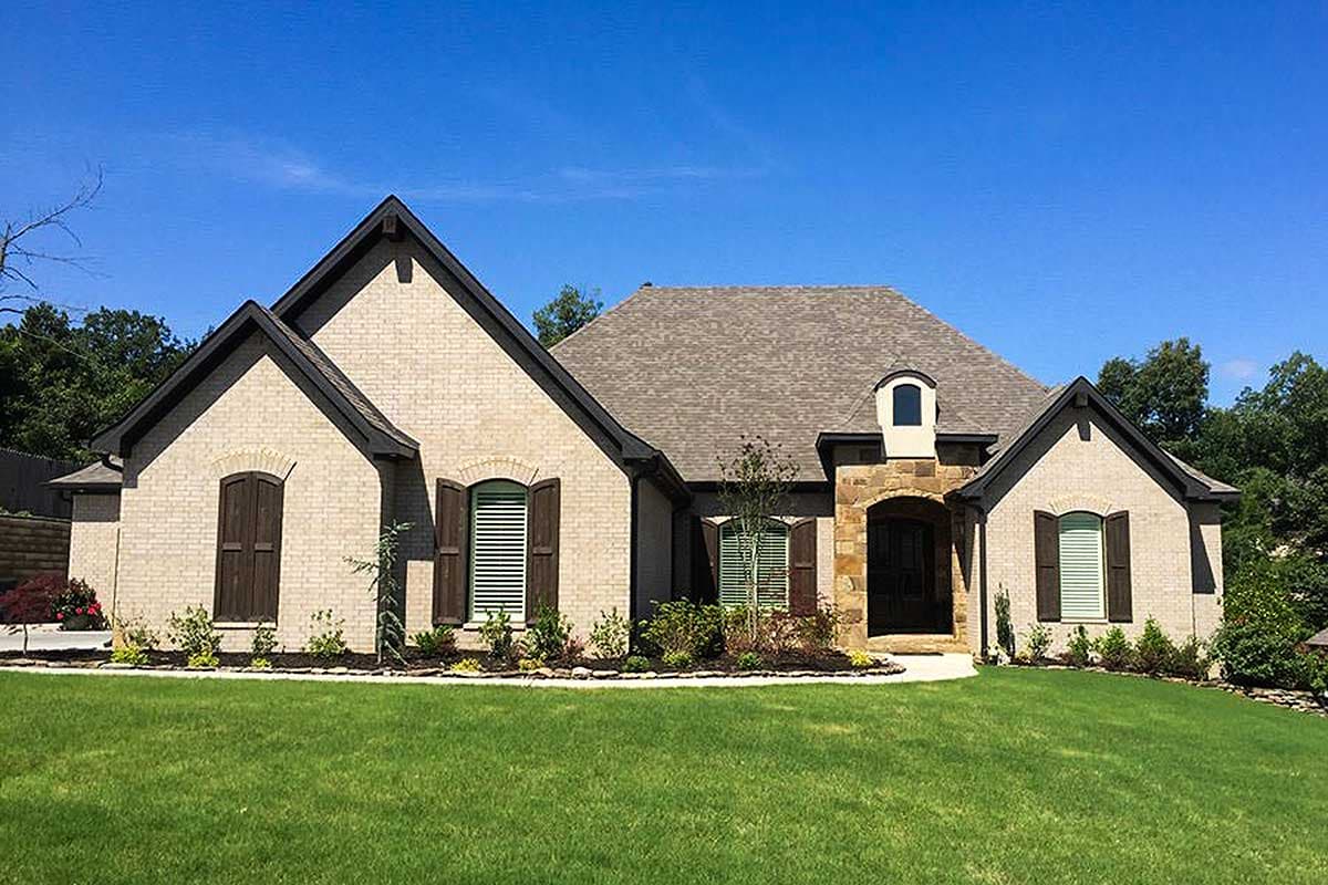 House plan exterior: One-story brick home with prominent gables, arched windows, stone-accented entry, and asphalt shingle roof.
