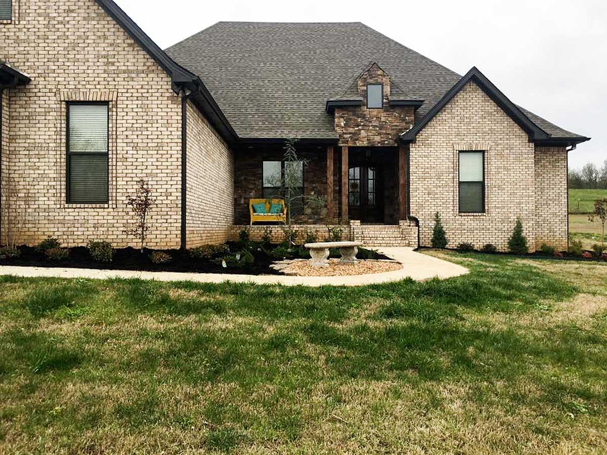 House plan exterior featuring light brick facade, gabled roof, stone accent, and covered entry porch with timber columns.