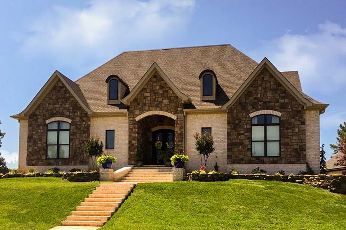 House plan exterior with stone and brick facade, gabled dormers, and arched entryway.