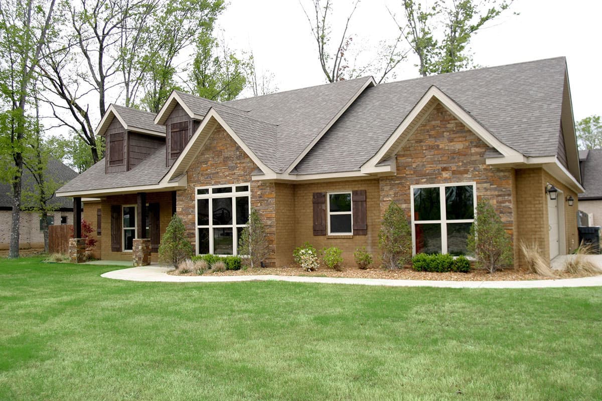 House plan exterior shows a one-story home with stone and brick facade, gables, dormers, and covered porch.