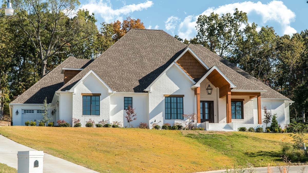 House plan exterior: One-story white brick home with gabled roofs, prominent entry portico, and attached garage.