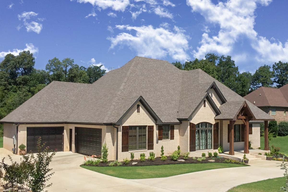 House plan exterior: one-story Modern style with multi-level roof, brick facade, three-car garage, and covered entry with exposed beams.