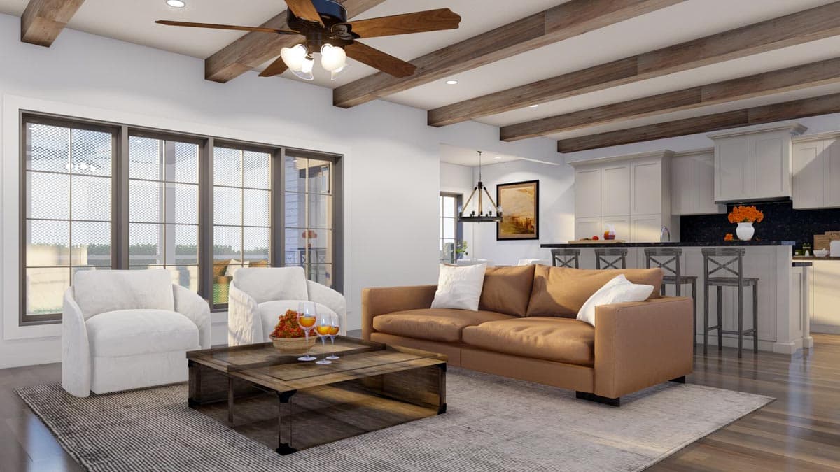 Great room with exposed beams, large windows, a tan sofa, two white armchairs, and an open kitchen with island seating.