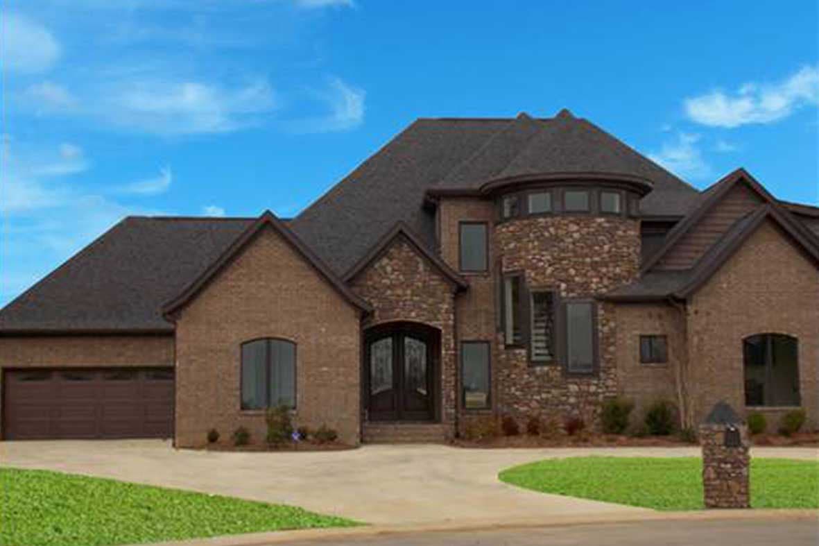 House plan exterior with brick facade, stone accents, double entry doors, and a circular tower with multiple windows.