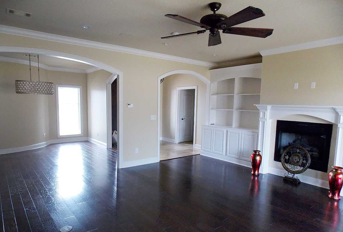 Interior view of a living room with dark hardwood floors, built-in bookshelves, fireplace, and arched doorways.