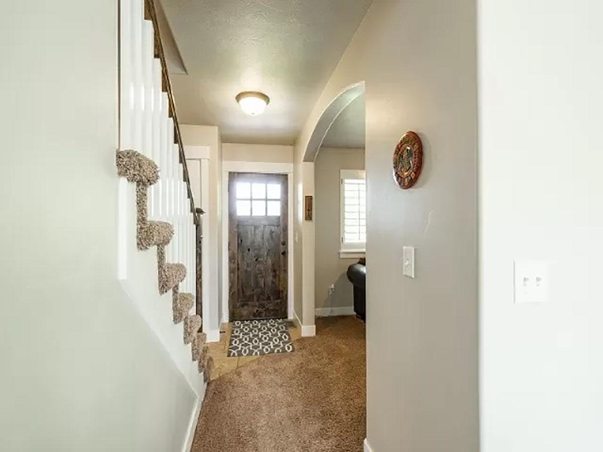 Interior view of a hallway with a carpeted staircase, a wood-paneled front door, and an arched doorway to another room.