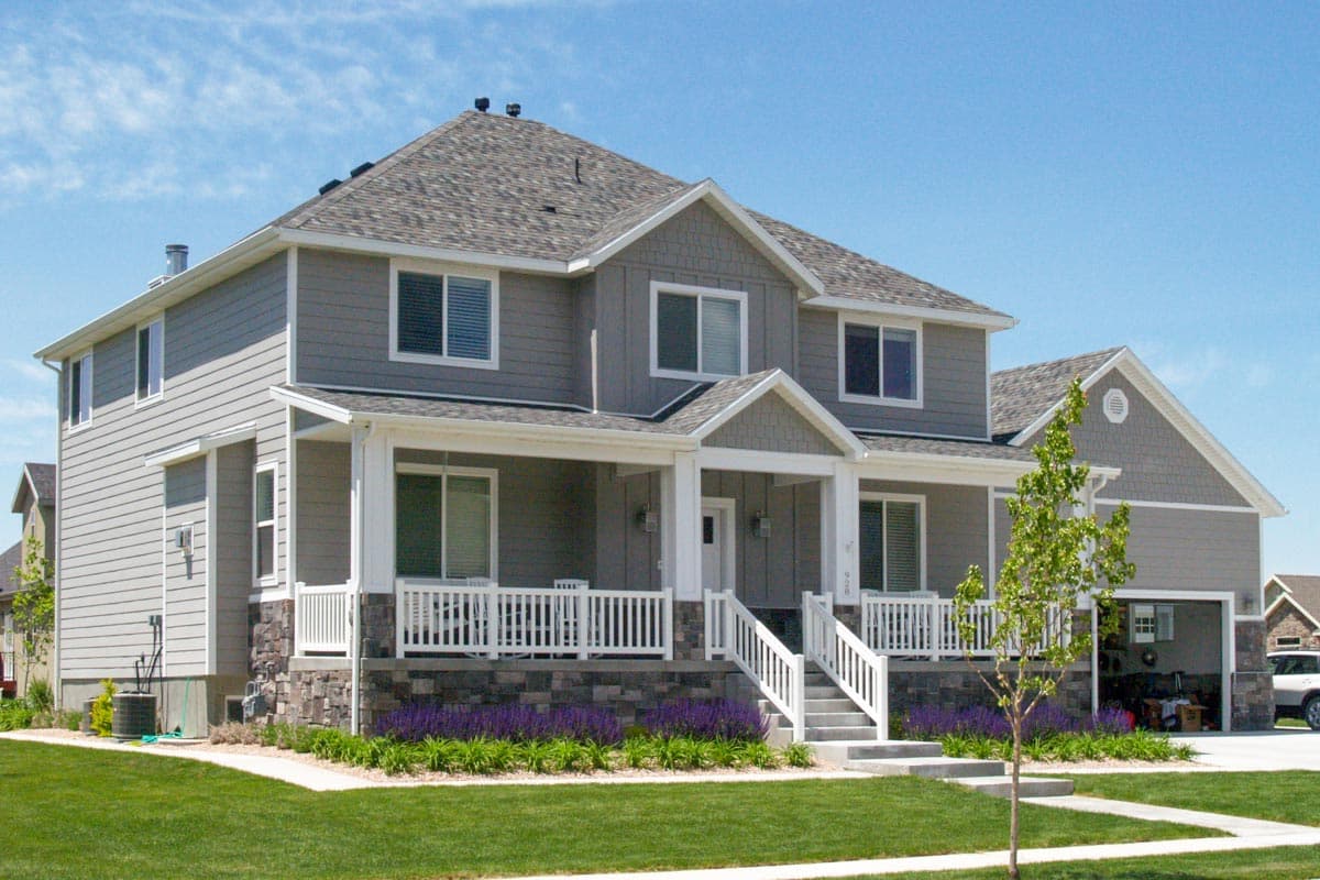 Two-story house plan exterior with a wraparound porch, stone accents, multiple gables, and an attached garage.