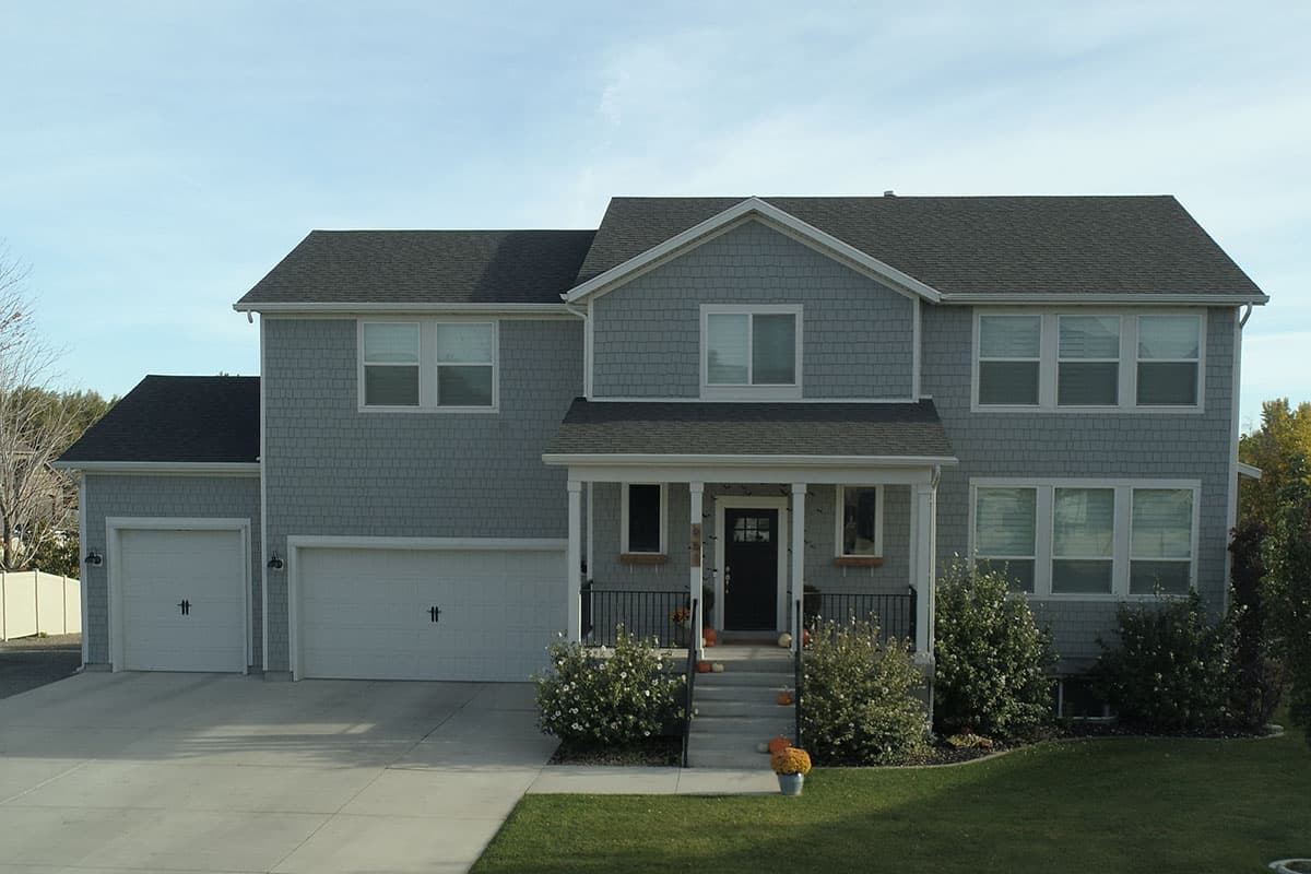 Two-story house plan exterior with gray shake siding, white trim, covered front porch, and a three-car garage.