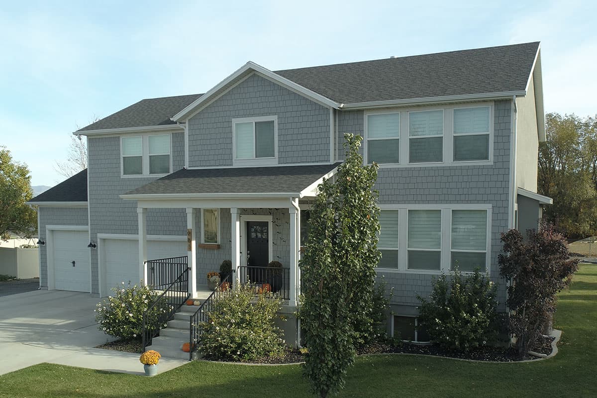 Two-story house plan exterior with gray shaker siding, a covered front porch, and a three-car garage.