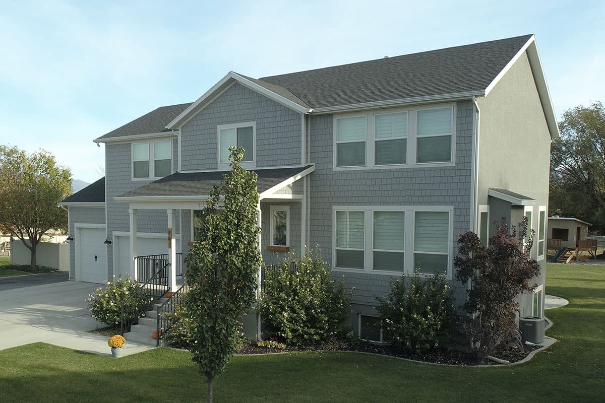 House plan exterior: Two-story home with shingle siding, prominent gables, covered front porch, and attached garage.