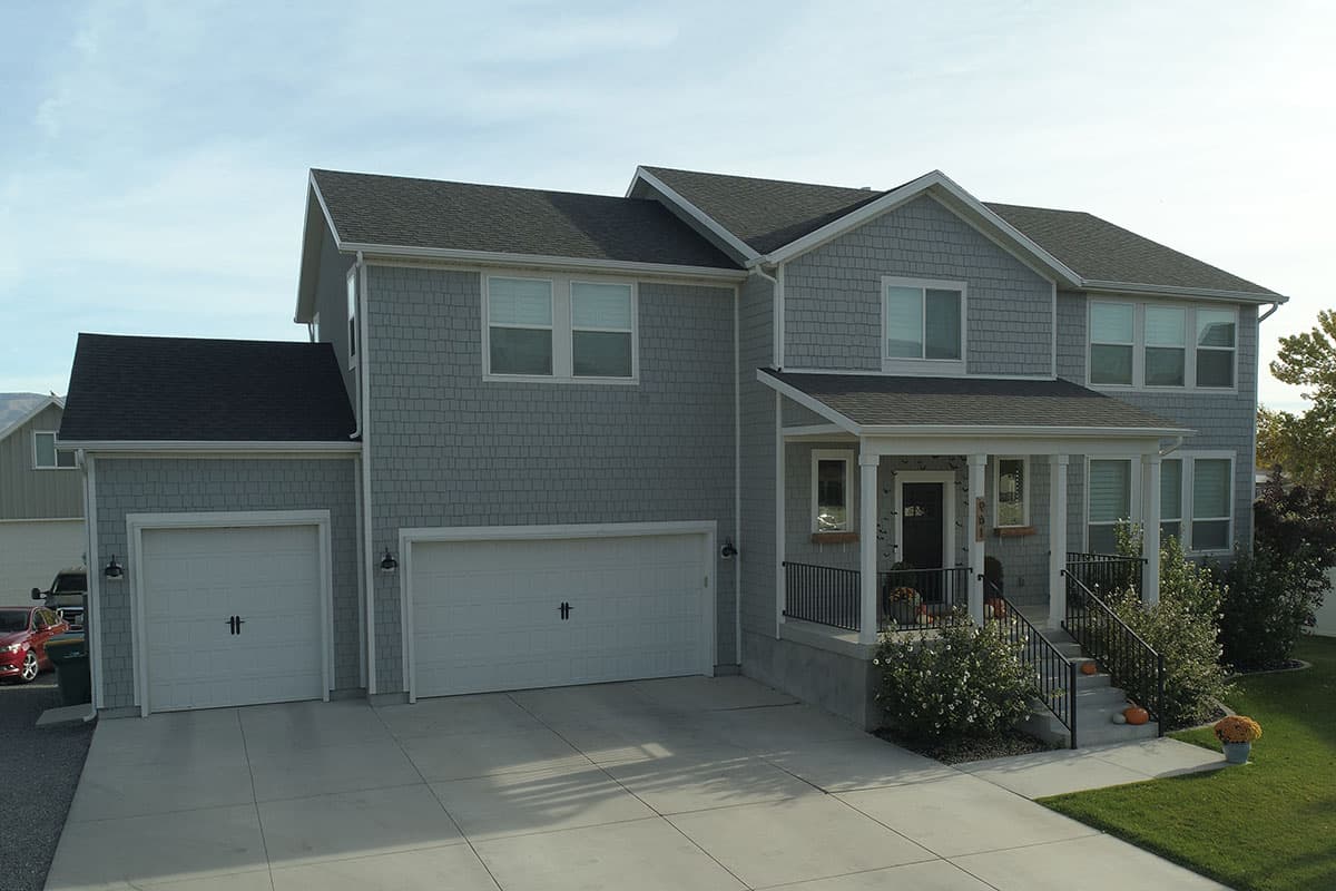 Two-story house plan exterior with a gabled roof, shingle siding, a covered front porch, and a three-car garage.