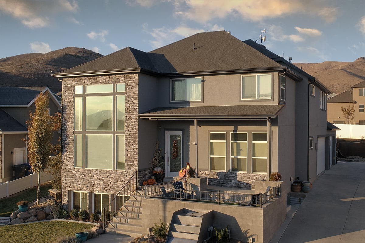 House plan exterior of two-story home with stacked stone accents, large grid windows, and a covered entrance with decorative autumn display.