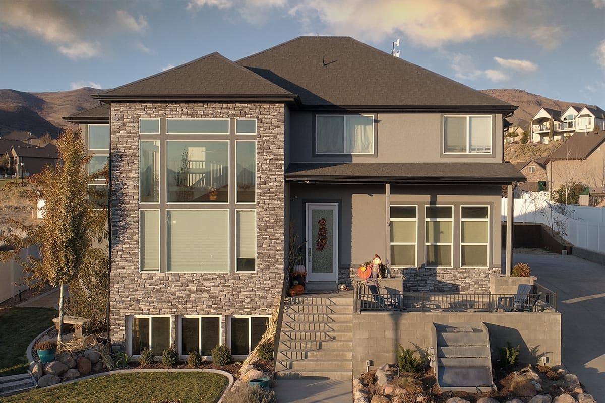 Two-story house plan exterior with stacked stone facade, large multi-pane windows, and covered porch.