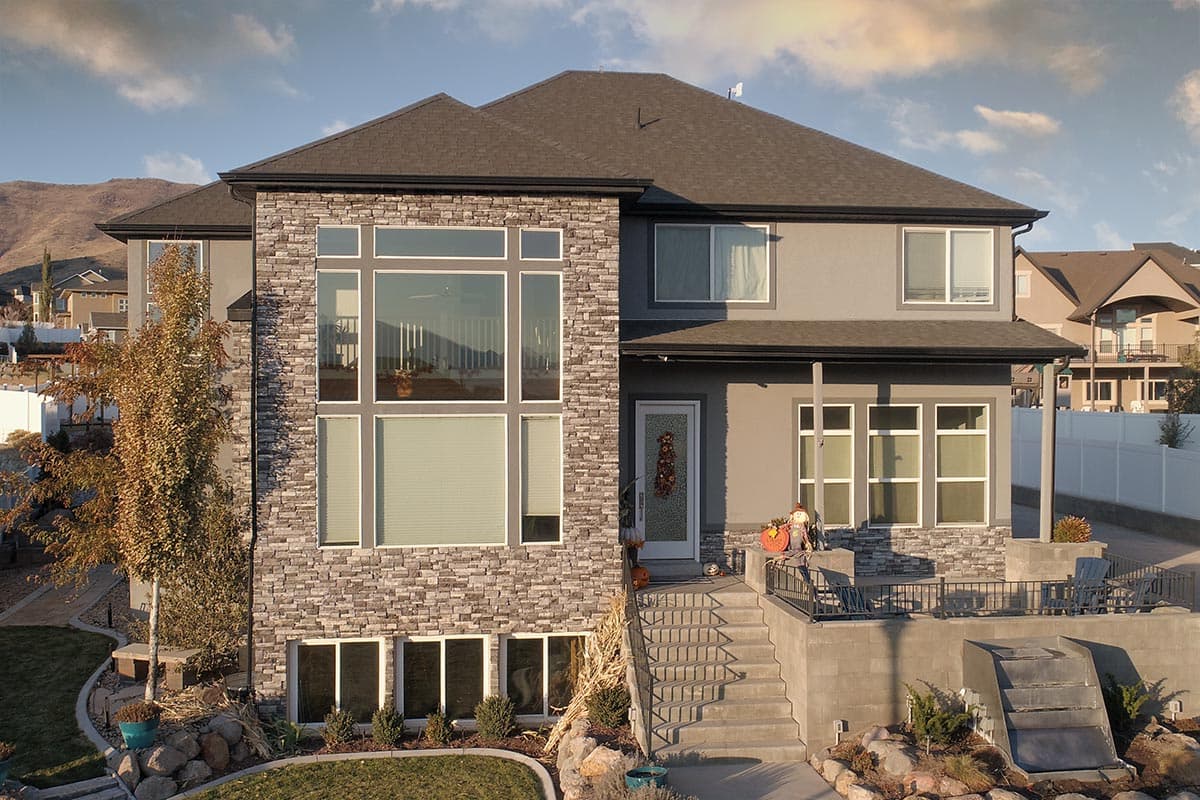 Two-story house plan exterior with stacked stone accents, large windows on main level, and a covered porch over the entrance.