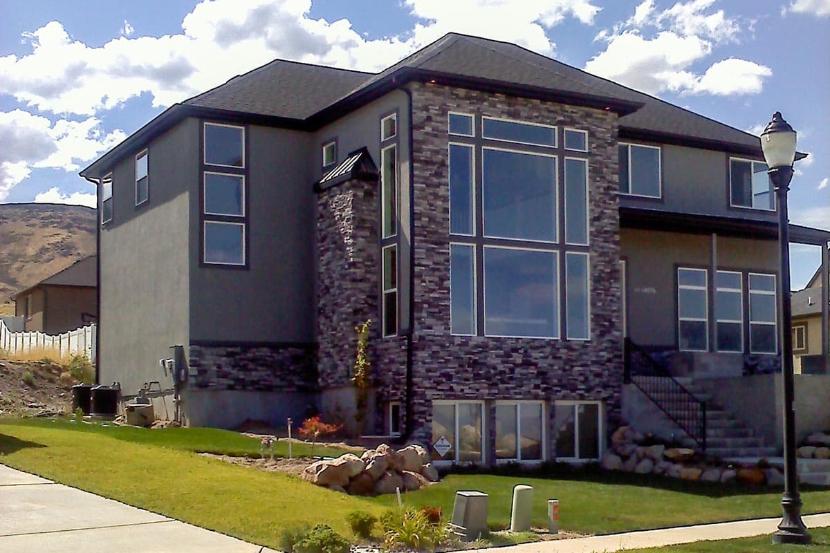 House plan exterior showing a modern two-story home with stucco siding, stacked stone accents, and large multi-pane windows.