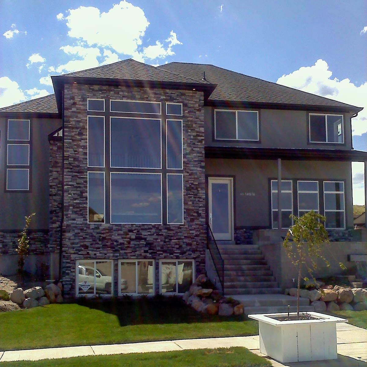 Two-story house plan exterior with stacked stone facade, large multi-pane windows, and dark pitched roof.