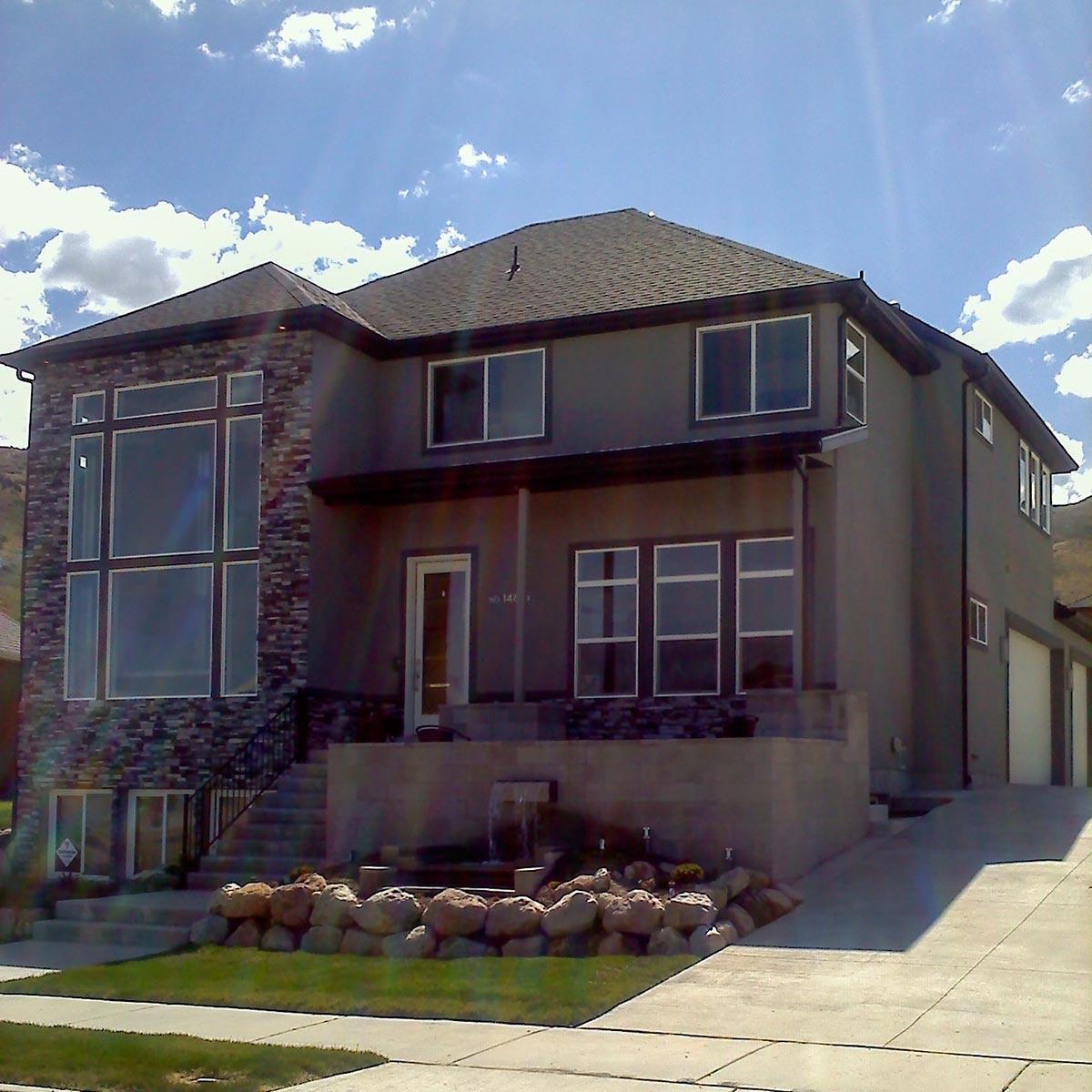 Two-story house plan exterior with large stone-clad window and covered porch with garage.