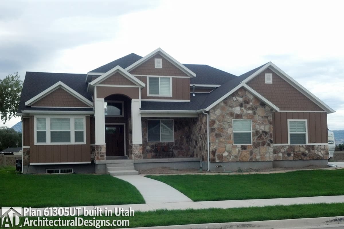 House plan exterior: two-story home with stone and wood siding, gables, dormers, and arched entryway.