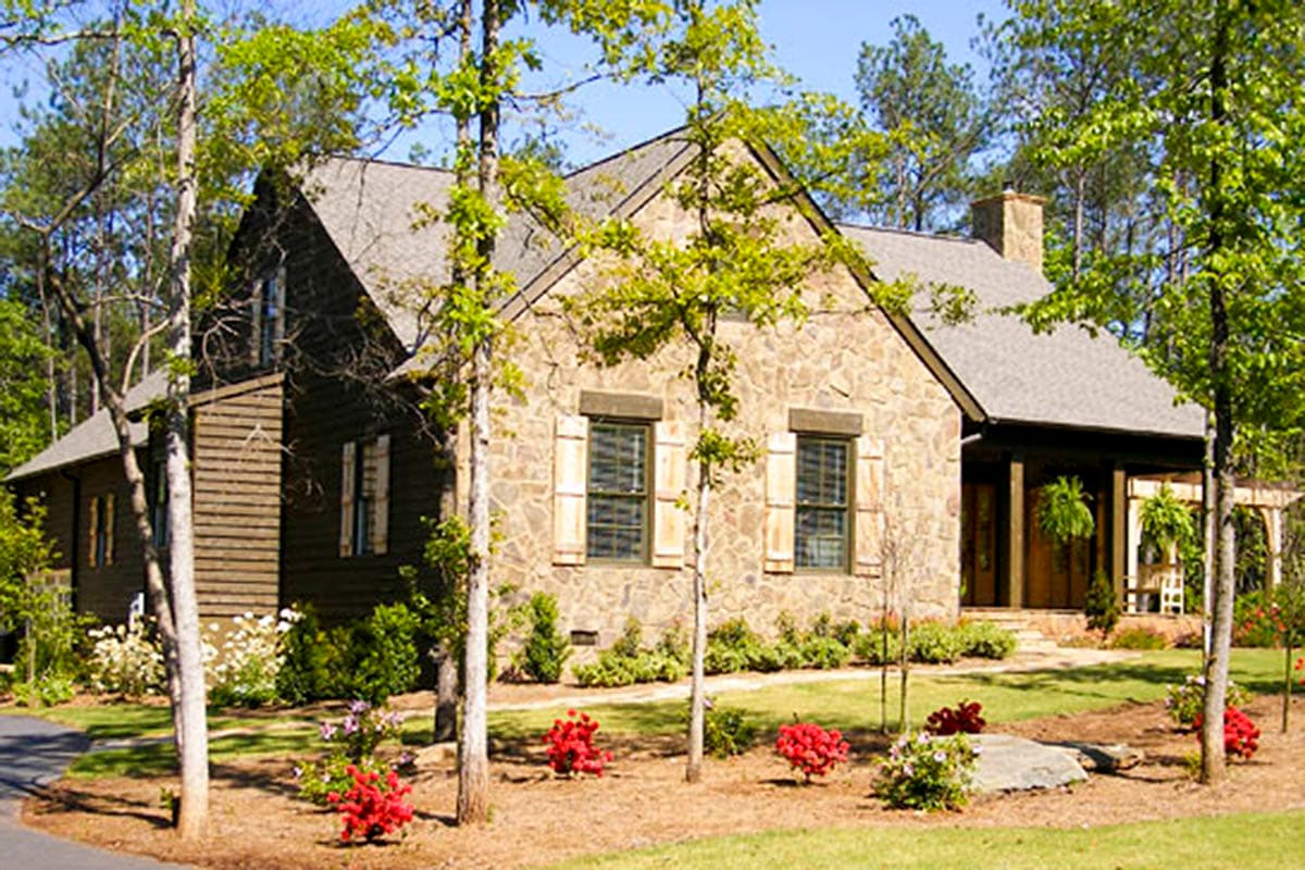 House plan exterior showing stone and wood siding, gable roof, dormers, and covered porch with stone chimney.