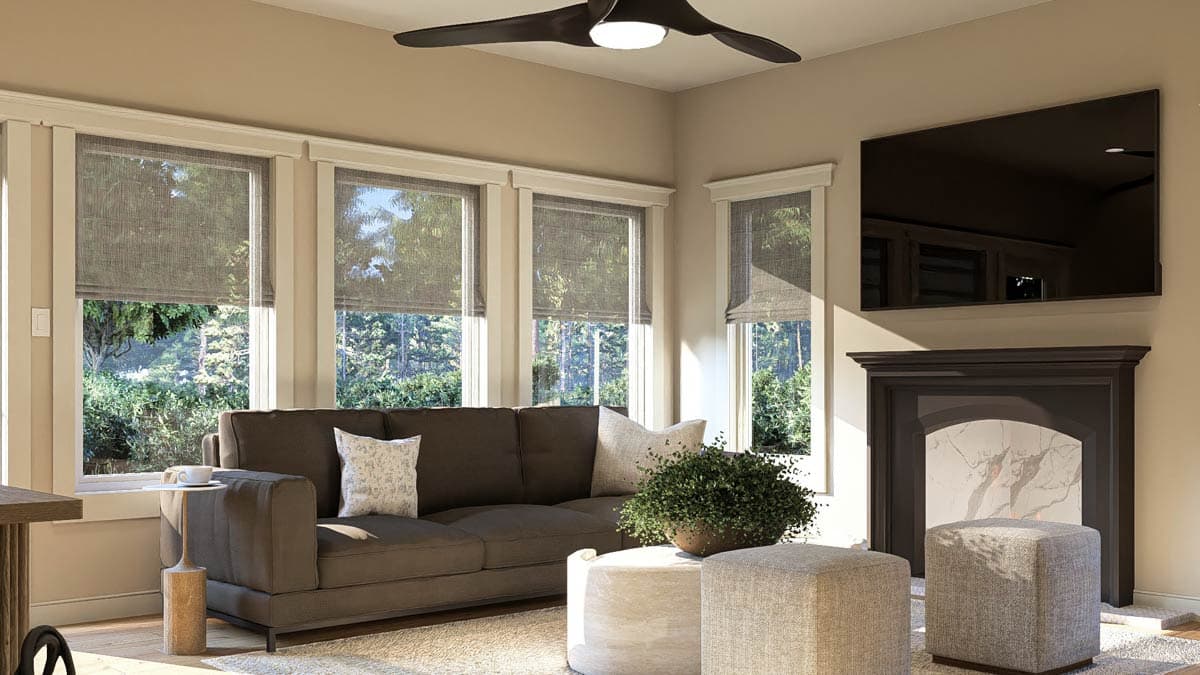 Living room with sofa, fireplace, mounted TV, ceiling fan, and large windows overlooking trees.