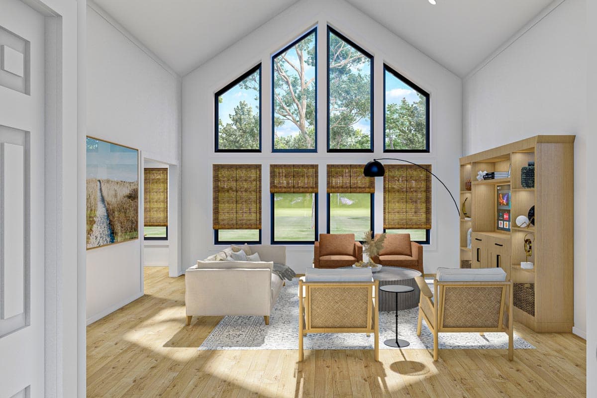 Modern living room with vaulted ceiling, floor-to-ceiling windows, sofa, chairs, and built-in shelving.