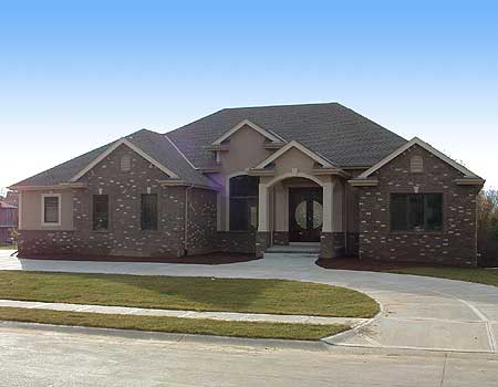 House plan exterior: A one-story residence with a brick facade, prominent arched entryway, multiple gables, and a dark asphalt shingle roof.