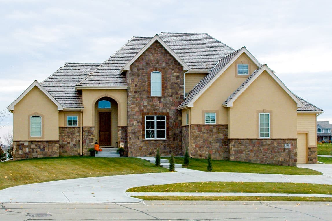 House plan exterior with stone accents, arched entry, multiple gables, and a shingled roof.