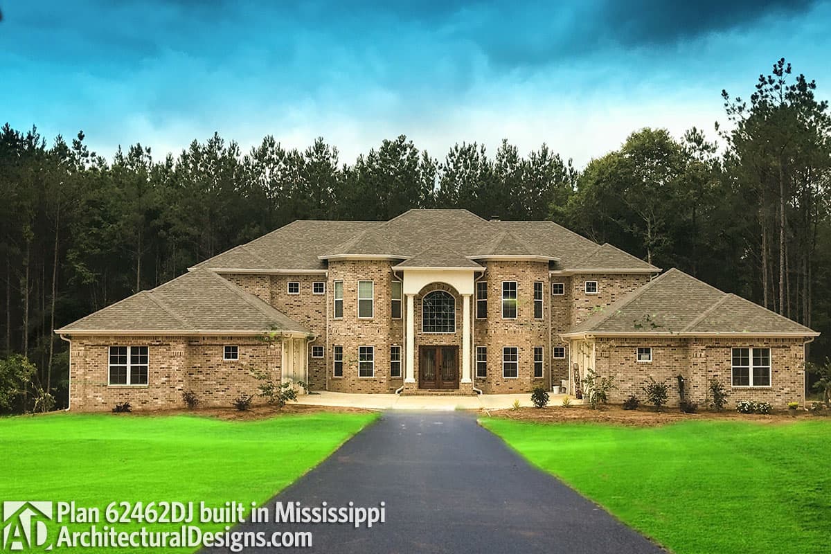 House plan exterior view of a two-story brick home with a central arched entryway, flanking wings, and hip roofs.