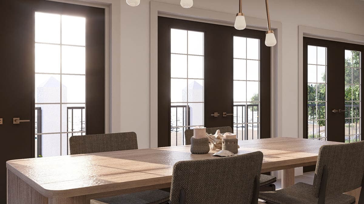 Dining room with wooden table, chairs, and three sets of French doors with grid panes looking out to water and trees.