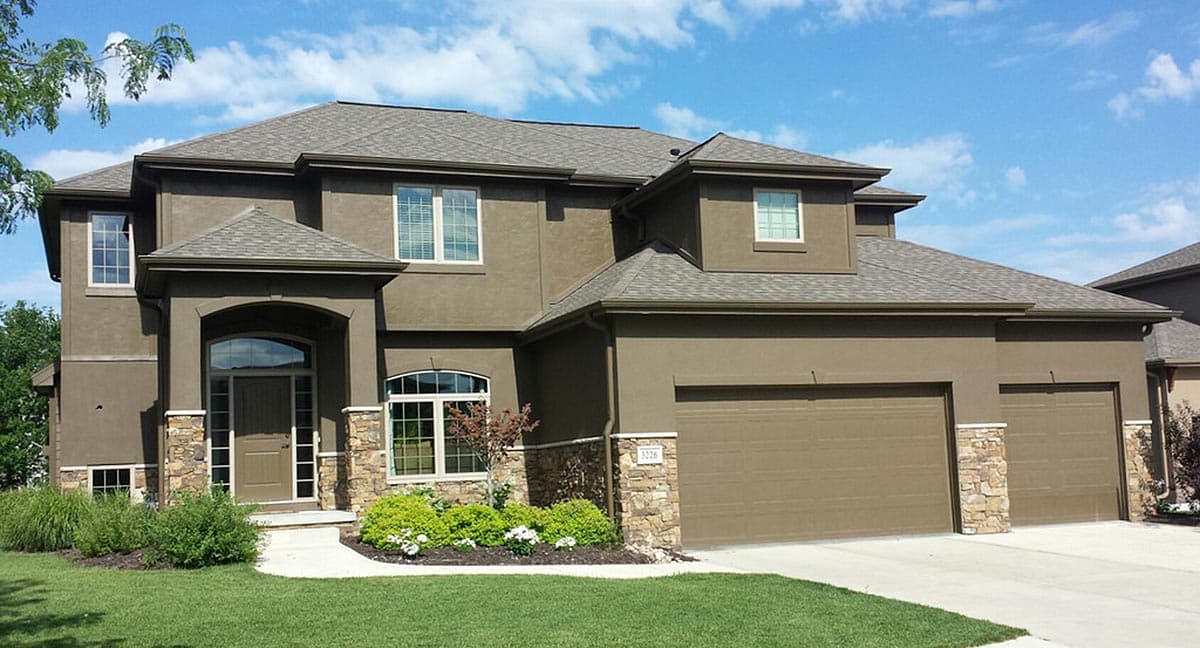 House plan exterior: Two-story home with stucco finish, arched entryway, stone accents, multiple gables, and a three-car garage.