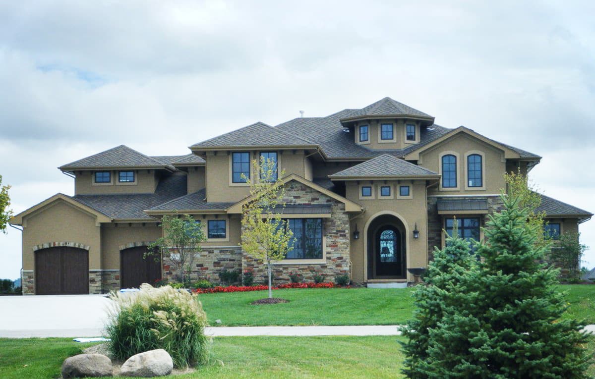 House plan exterior with stone accents, arched entryway, multiple gables, and a three-car garage.