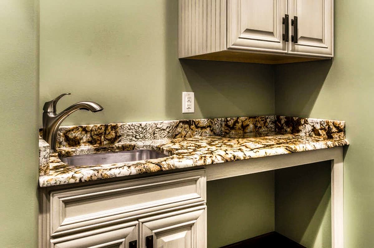 Wet bar with stainless steel sink, granite countertop, and distressed wood cabinetry. Includes upper cabinets and an open shelf.