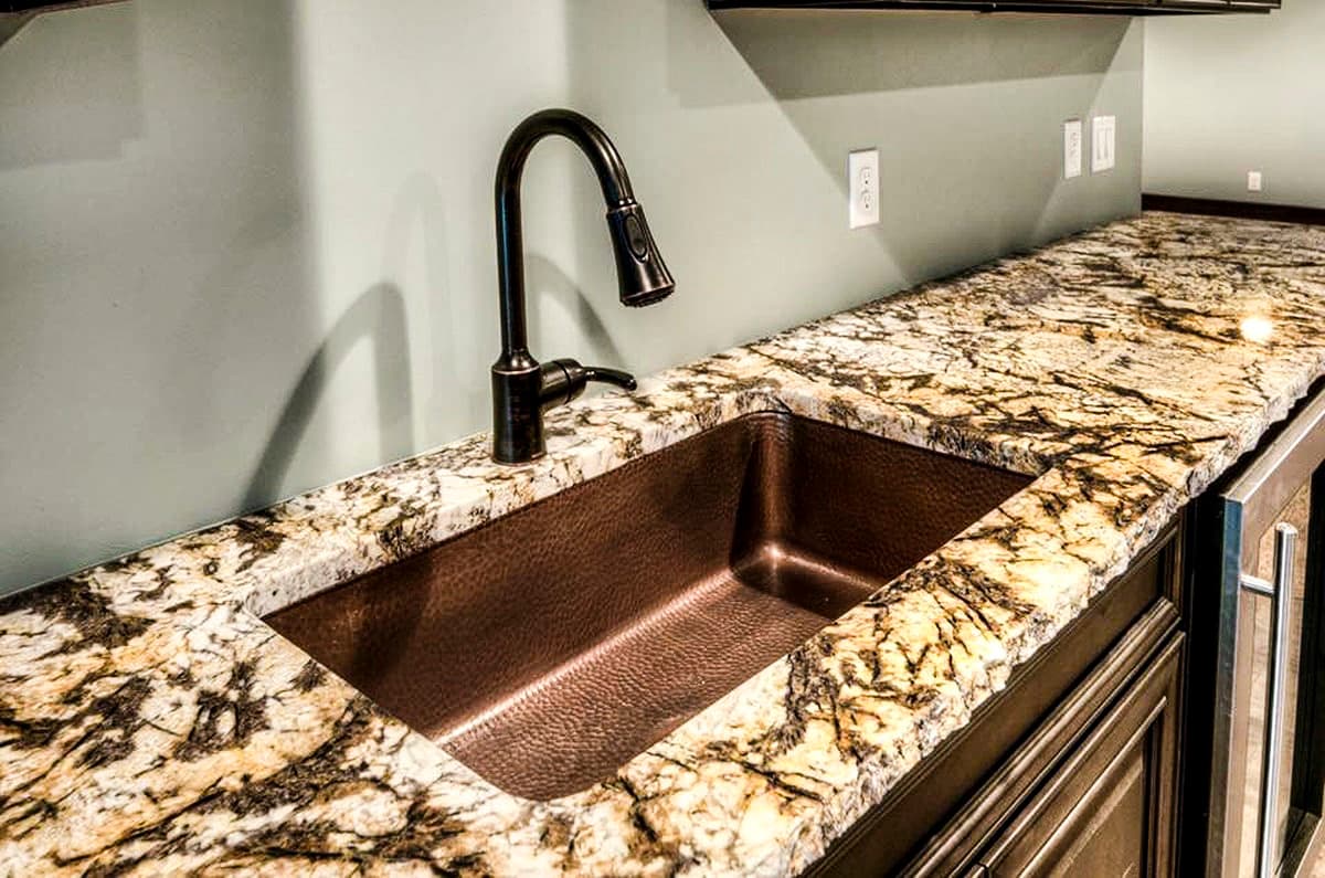 Undermount copper sink with a gooseneck faucet on granite countertop, adjacent to dark wood cabinetry.