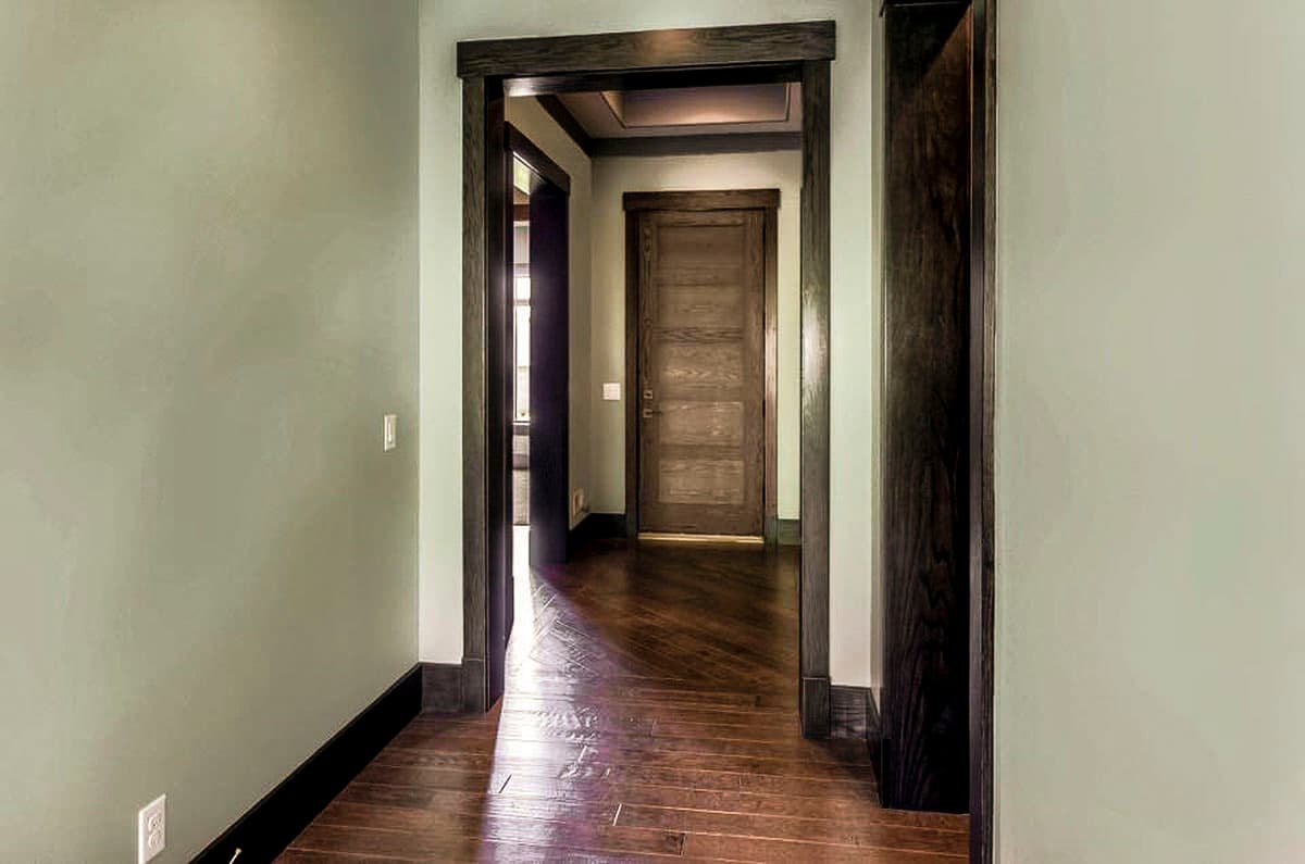 Hallway with dark wood trim, five-panel door, and hardwood floors.