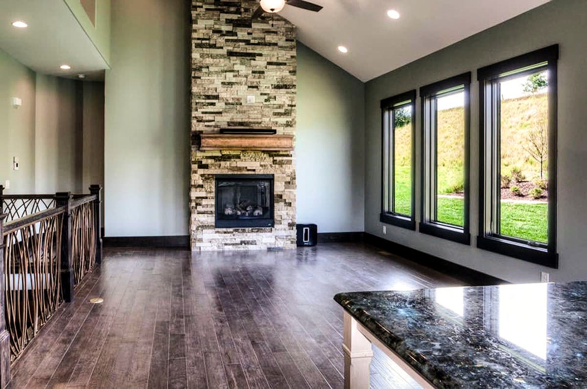 Interior view of a great room with a floor-to-ceiling stone fireplace, vaulted ceiling, and three large windows.