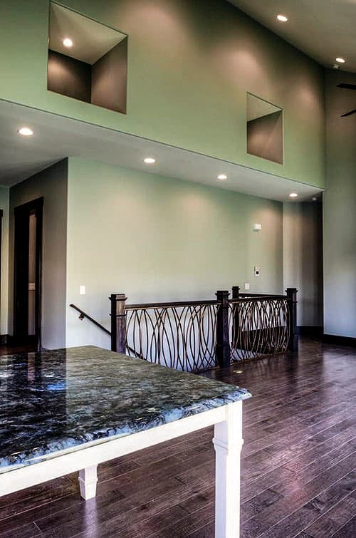Interior view of a house with a two-story open concept, decorative metal railing on a staircase, and recessed wall niches.