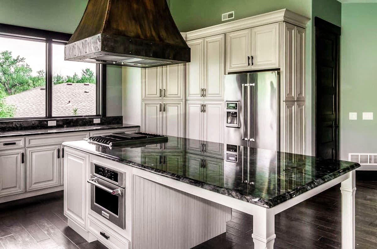Kitchen featuring a large island with stovetop, stainless steel appliances, custom cabinetry, and a metal range hood.
