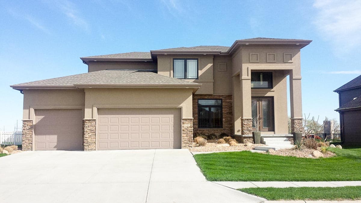 House plan exterior: Two-story modern home with stucco finish, stone accents, three-car garage, and prominent entry.