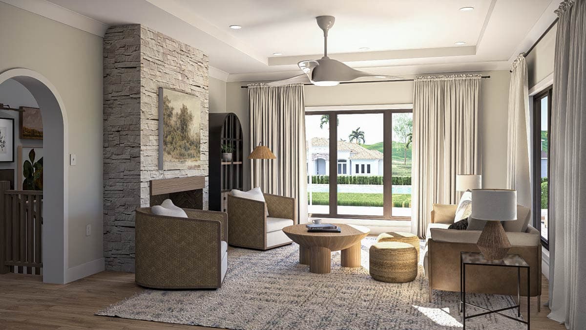 Living room with stone fireplace, tray ceiling, modern fan, and large windows overlooking backyard.
