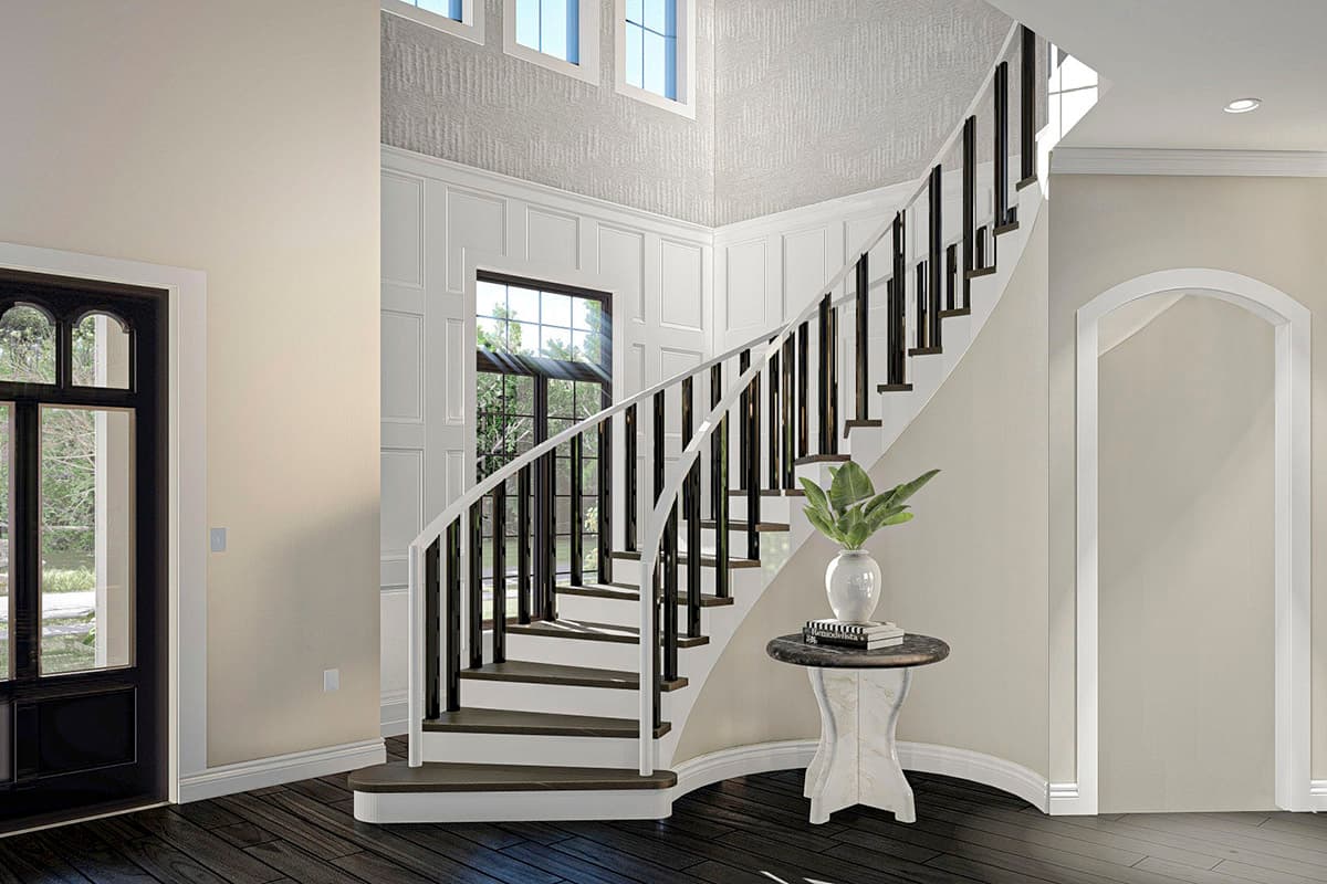 Interior view of a house: curved staircase with dark spindles, white railing, wainscoting, and arched doorway.