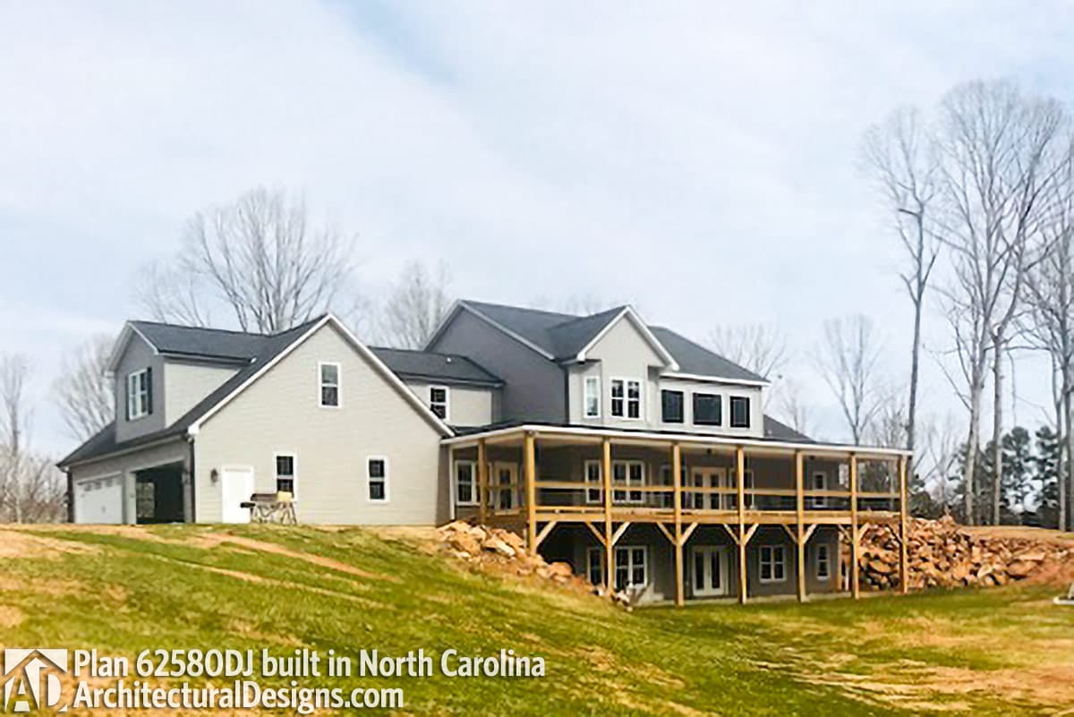 House plan exterior with two stories, side-entry garage, and wraparound covered deck on a sloped lot.