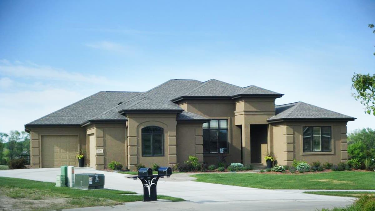 House plan exterior for a one-story home with a two-car garage, hip roof, arched window, and covered entryway.