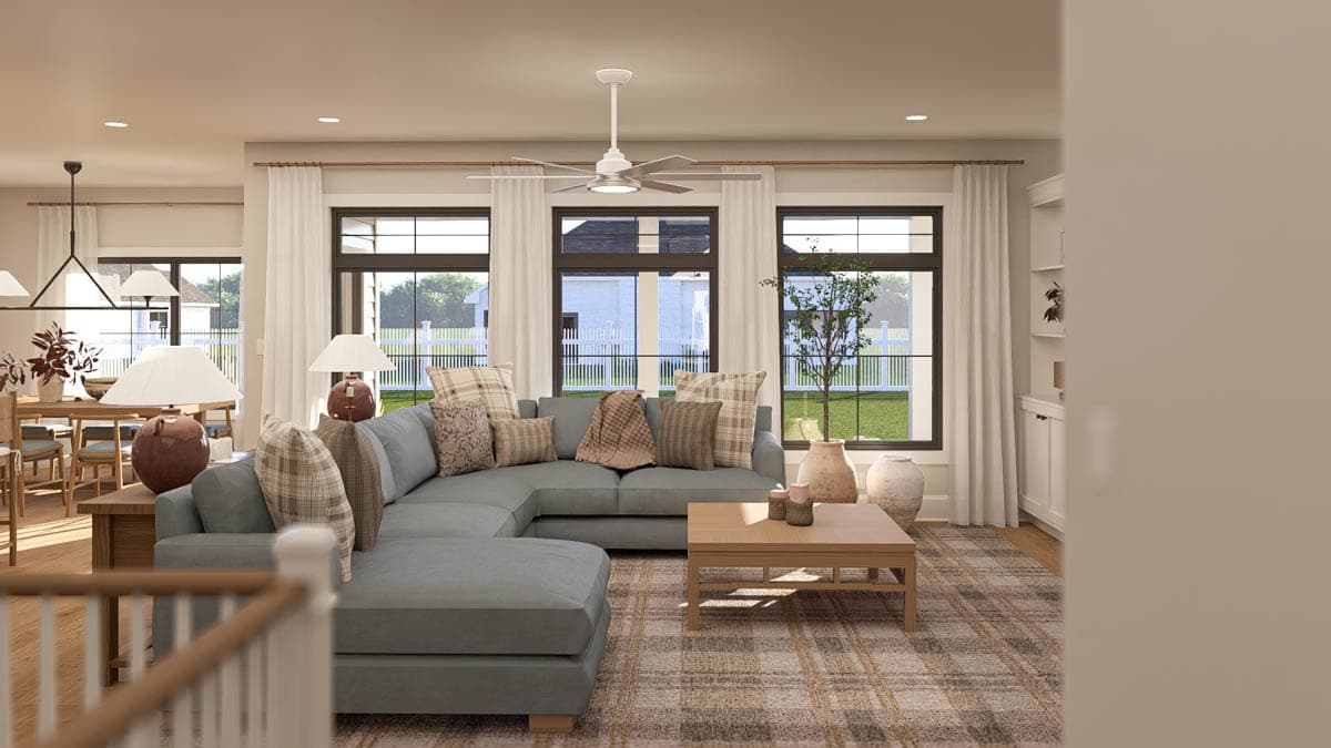 Living room with L-shaped sectional sofa, coffee table, ceiling fan, and large windows overlooking a yard with white fence.