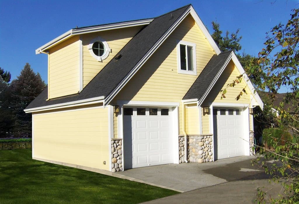 House plan exterior: Two-story building with a two-car garage, gabled roof, round window, and stone accents.