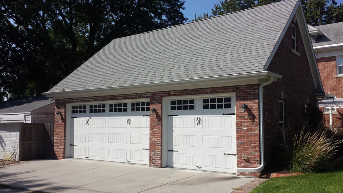 House plan exterior shows a brick two-car garage with white panel doors, divided windows, and a gambrel roof.