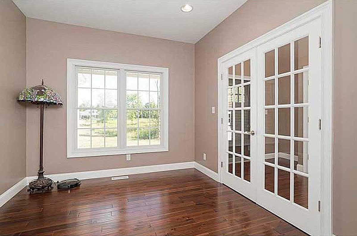 Interior view of a room with white French doors, a large multi-pane window, and hardwood floors.